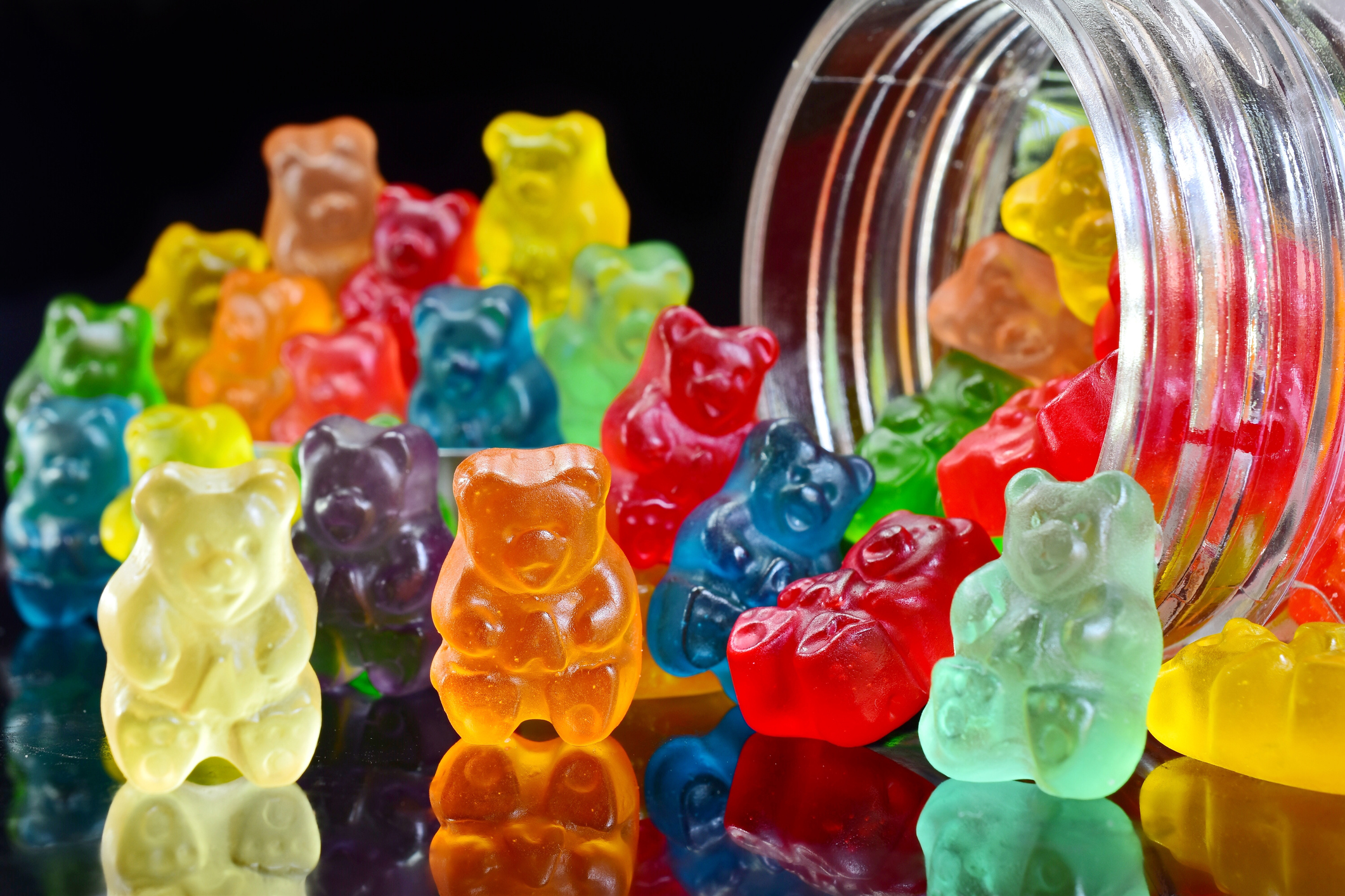 Open glass jar on its side with colorful gummy bears spilling out