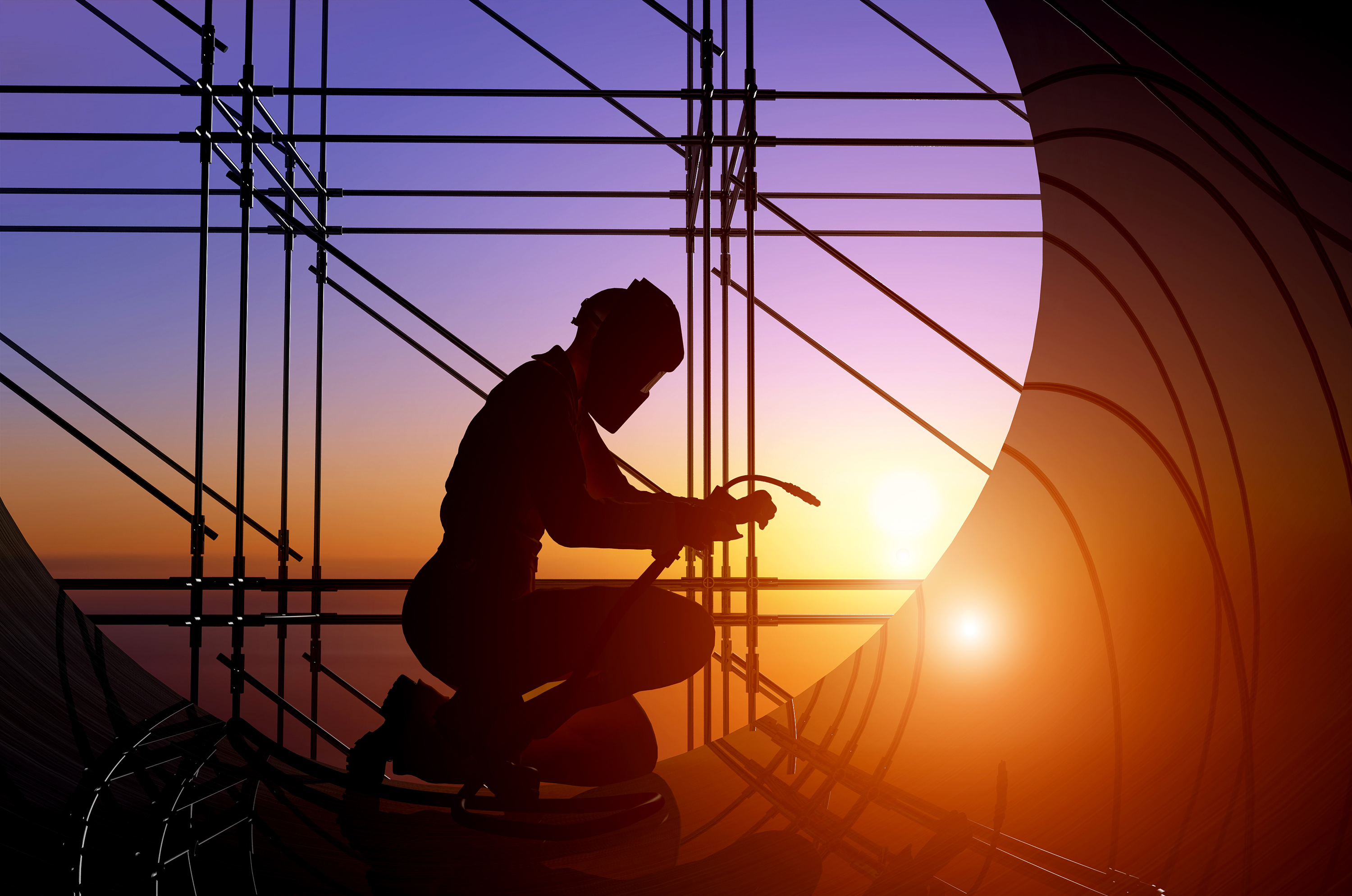 Silhouette of a welder working on site with a sunset in the background